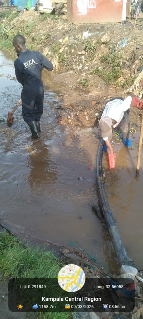 KCCA workers use shovels and gloves to clear debris from a muddy drainage ditch.