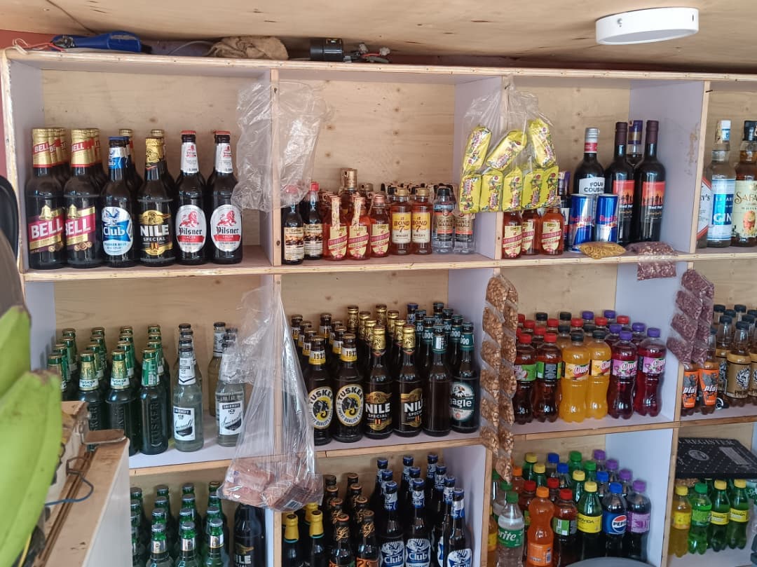 Wooden shelves stocked with various bottled beers, liquors, sodas, and snacks in a shop.